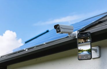 Modern solar-powered security camera with attached solar panel mounted on a home exterior, capturing live footage on a smartphone screen, symbolizing smart home integration and sustainable energy.