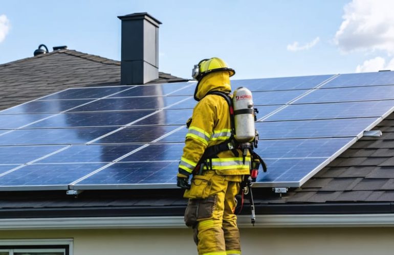 Professional firefighter demonstrating specialized safety techniques for combating fires on modern solar panel rooftop installations, highlighting safe water application and strategic firefighting equipment.